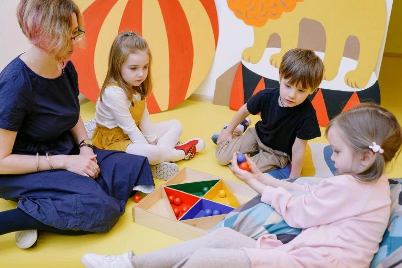 a woman sitting on the floor with a group of children, pexels contest winner, interactive art, softplay, profile image, cutecore clowncore, four hands