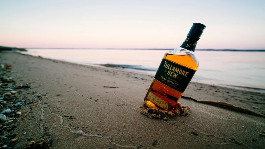 a bottle of whiskey sitting on top of a sandy beach, on a beach