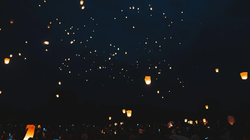 a group of people standing in front of a sky filled with lanterns, pexels contest winner, light and space, background image, summer festival night, fire flies, ☁🌪🌙👩🏾