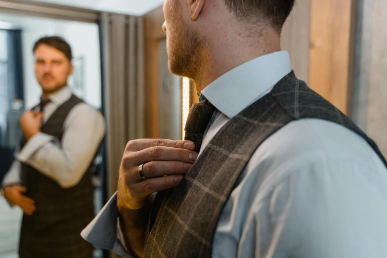 a man adjusting his tie in front of a mirror, inspired by George Henry, pexels contest winner, tartan garment, extra detail, wearing jewellery, from back