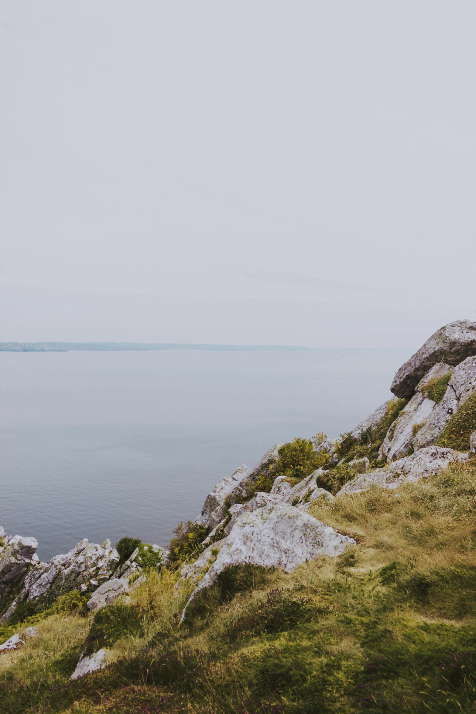 a man standing on top of a cliff next to a body of water, panorama distant view, ireland, low quality photo, conor walton