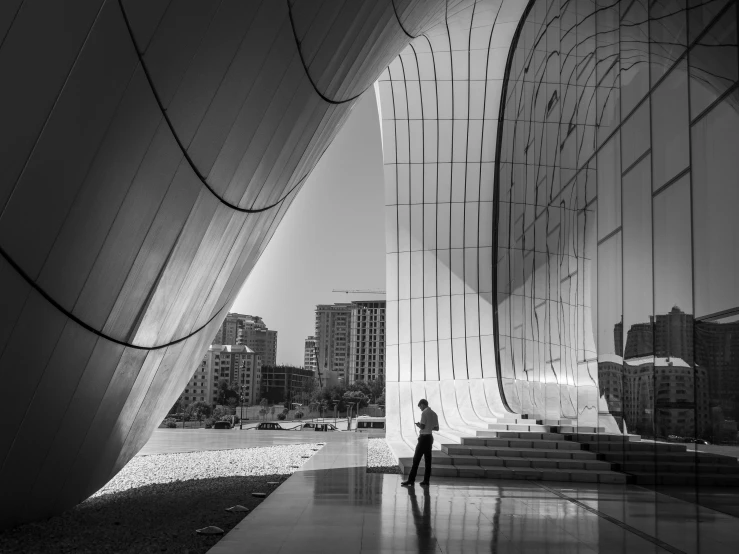 a black and white photo of a person standing in front of a building, by Farid Mansour, unsplash contest winner, conceptual art, sweeping arches, glossy reflections, concert hall, morning light