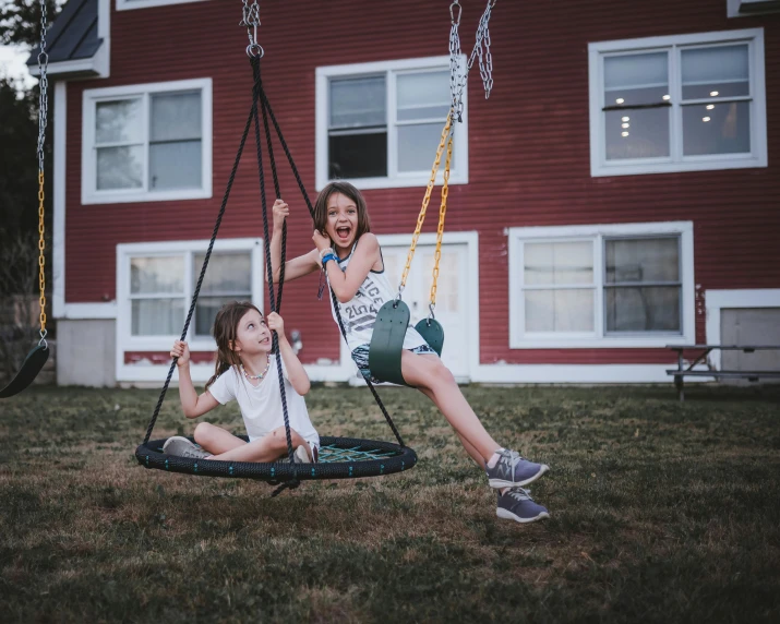 two girls on a swing in front of a house, by Matt Cavotta, pexels contest winner, epic. 1 0 0 mm, very round, ground - level medium shot, mid air shot