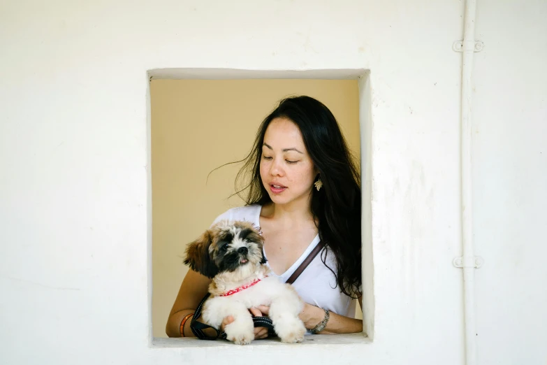 a woman holding a small dog in her arms, a portrait, by Julia Pishtar, pexels contest winner, happening, looking through a window frame, jamie chung, shih tzu, vietnamese woman