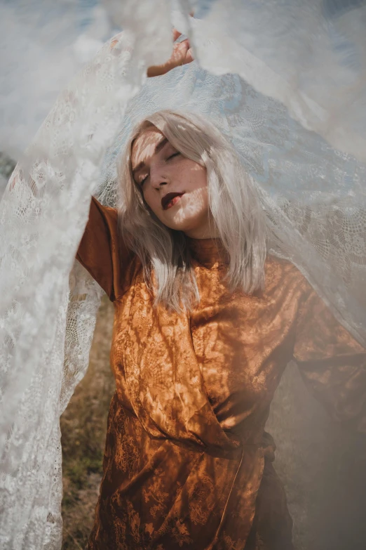 a woman standing in a field with a veil over her head, an album cover, inspired by Elsa Bleda, trending on unsplash, aestheticism, flowing silver hair, orange robe, transparent body, concert