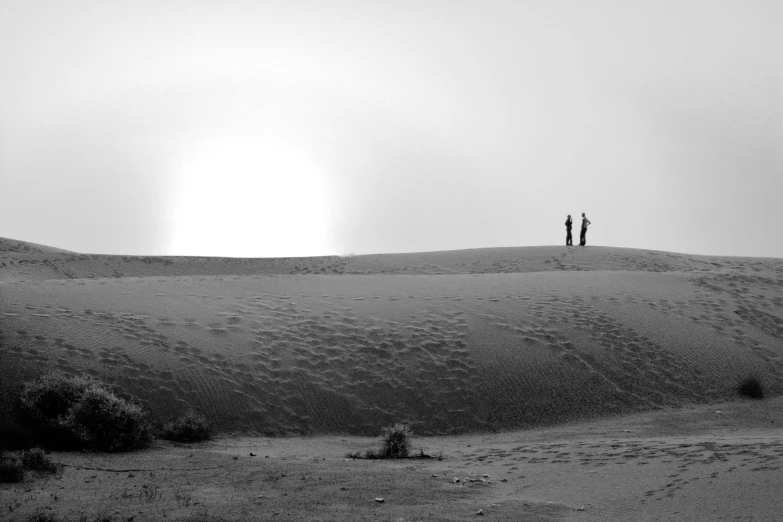 two people standing on top of a snow covered hill, a black and white photo, by Ismail Acar, pexels contest winner, sand desert, in the desert beside the gulf, actual photo, visible from afar!!