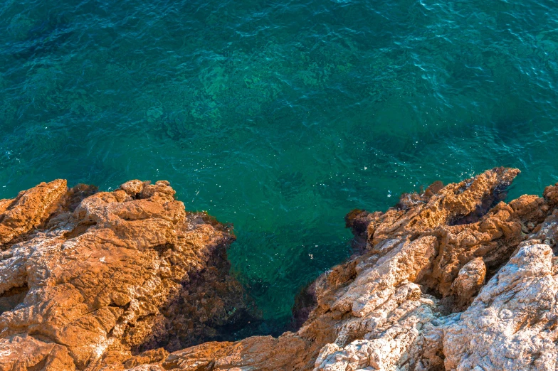 a man standing on top of a rock next to the ocean, pexels contest winner, les nabis, ocher and turquoise colors, down there, copper and emerald, thumbnail