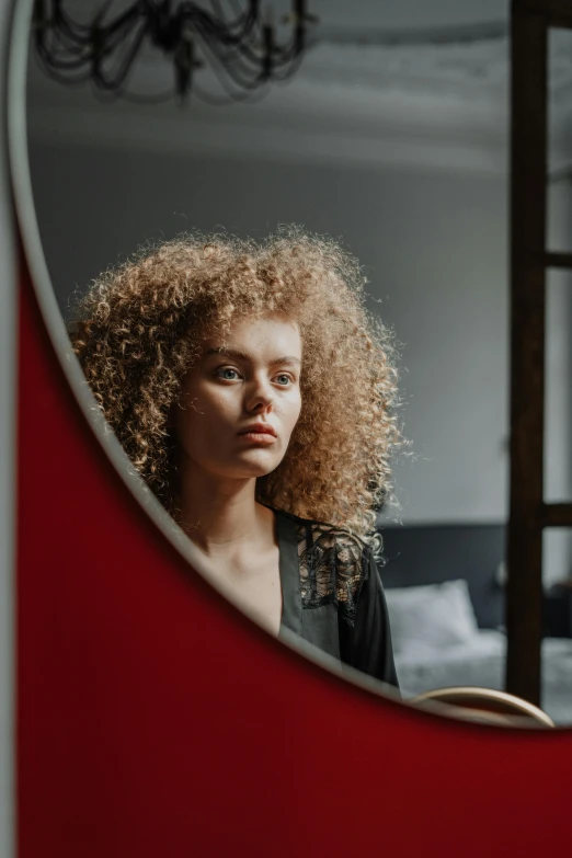 a woman with curly hair standing in front of a mirror, trending on pexels, red door blonde, 4 k asymmetrical portrait, frizzy hair, high resolution image