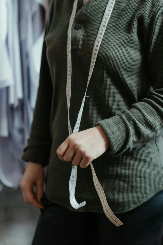 a woman with a measuring tape around her waist, by Nina Hamnett, trending on pexels, wearing a grey hooded sweatshirt, olive green, inspect in inventory image, ribbon