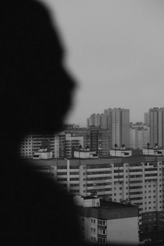 a black and white photo of a person looking out a window, a black and white photo, unsplash, realism, pyongyang city, city background in silhouette, album cover, stacked image