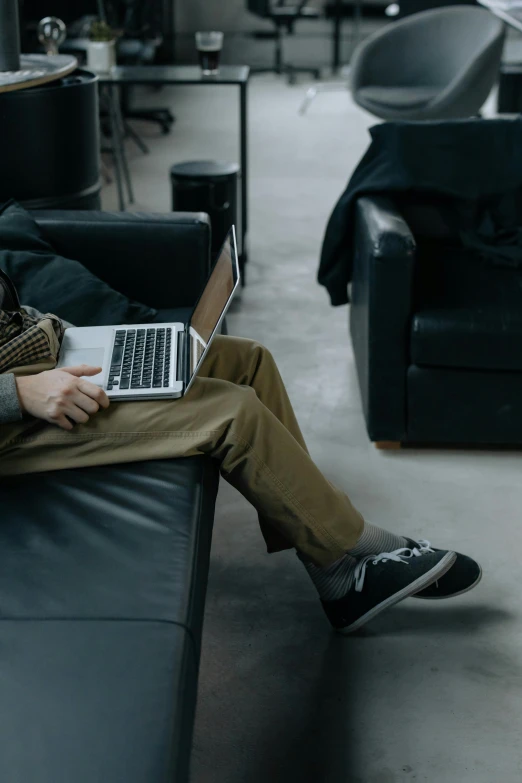 a man sitting on a couch with a laptop, trending on pexels, office clothes, non-binary, leather couch, performance