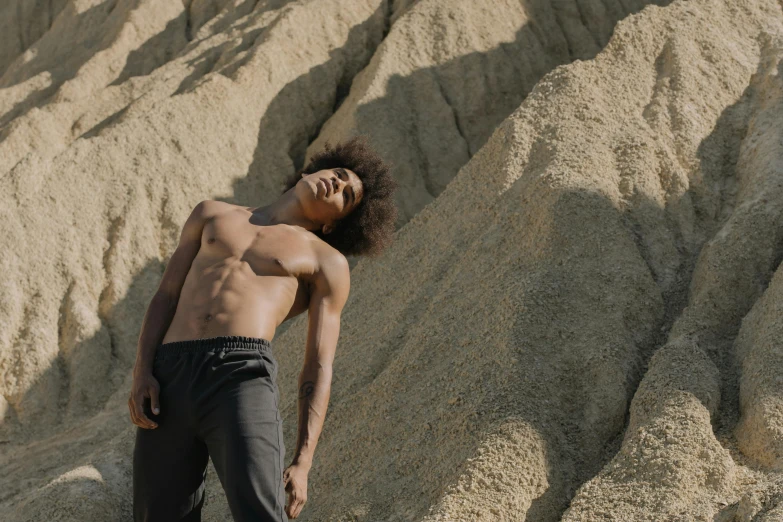 a man standing in front of a mountain of sand, trending on pexels, figuration libre, shirtless :: high detail, black teenage boy, afro, non binary model