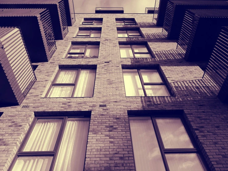 a tall brick building with lots of windows, inspired by Elsa Bleda, unsplash, sepia, purple, ten flats, low-angle