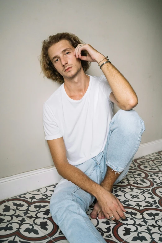 a man sitting on the floor talking on a cell phone, an album cover, unsplash contest winner, photorealism, plain white tshirt, wavy hair spread out, ( ( ( wearing jeans ) ) ), confident relaxed pose