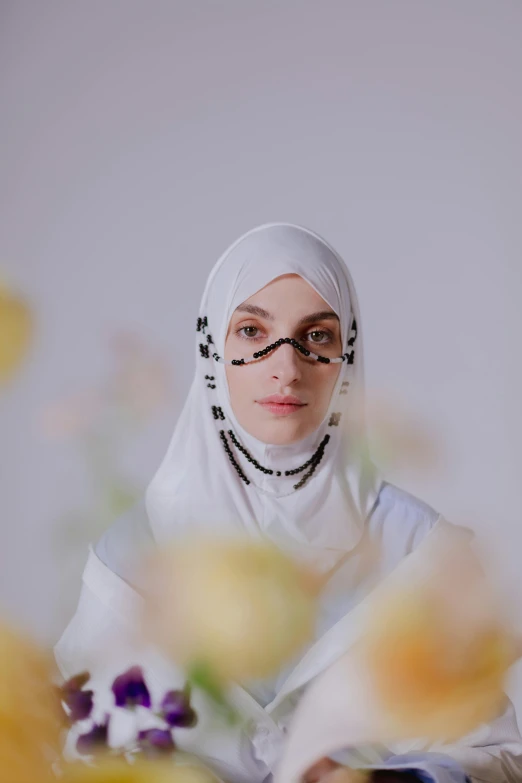 a woman in a white hijab sitting in front of flowers, an album cover, shot with sony alpha 1 camera, white facepaint, still from a movie, hziulquoigmnzhah