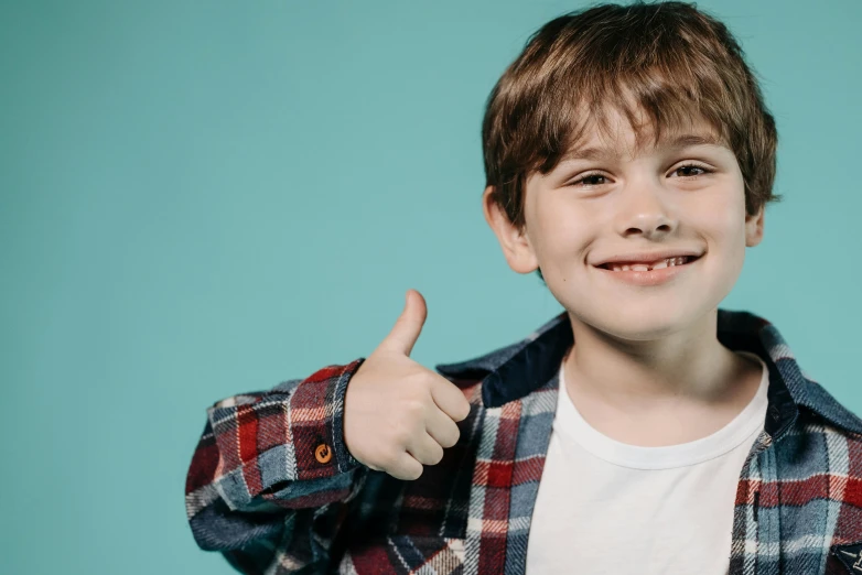a young boy giving the thumbs up sign, an album cover, pixabay, wearing a plaid shirt, portrait of a smiling, with a blue background, thumbnail