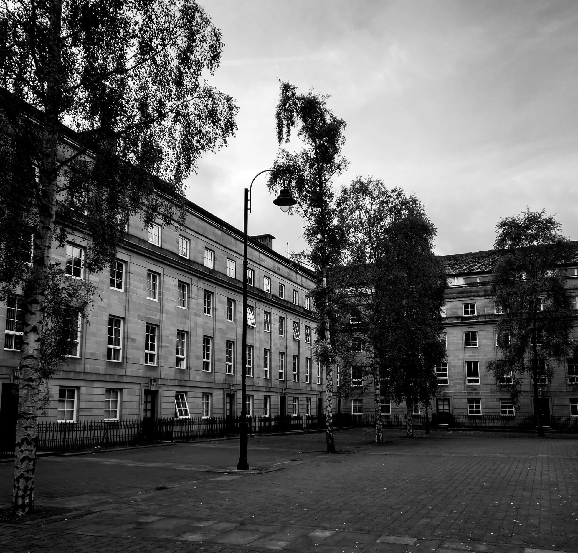 a black and white photo of a courtyard, a black and white photo, unsplash, barracks, glasgow, outdoors european cityscape, trees around