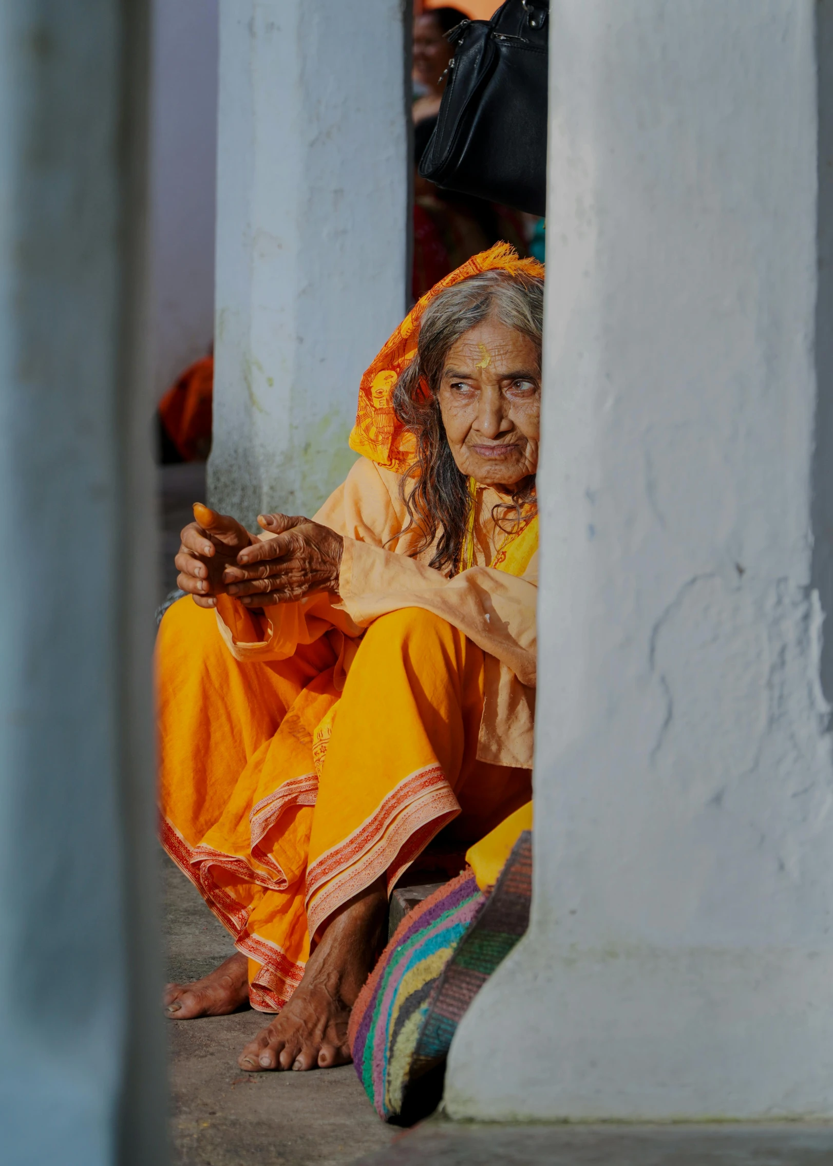 a woman sitting on the ground next to a pillar, a portrait, by Rajesh Soni, pexels contest winner, wise old indian guru, orange robe, a very macular woman in white, color photograph portrait 4k