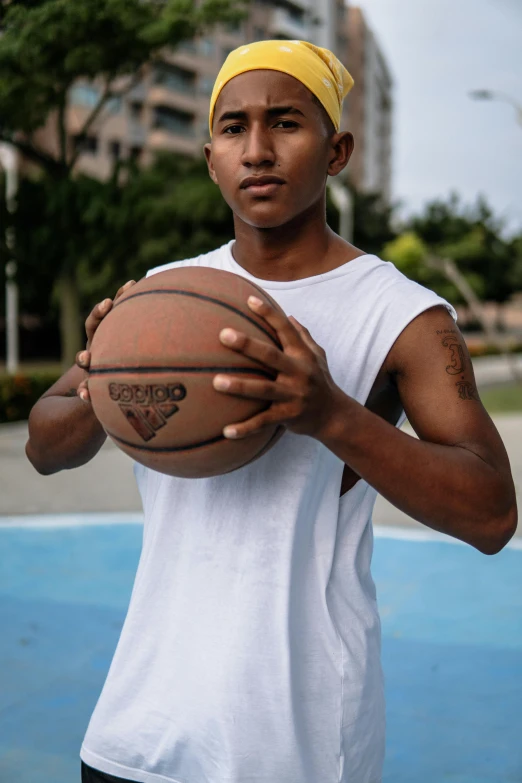 a man holding a basketball on a basketball court, south east asian with round face, wearing : tanktop, cement, androgynous male