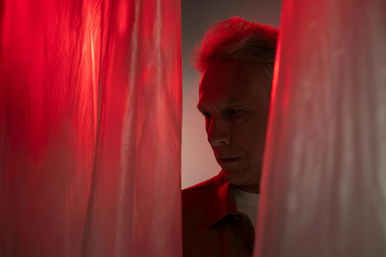 a man standing in front of a red curtain, detailled light, photographic still, silver red, looking around a corner