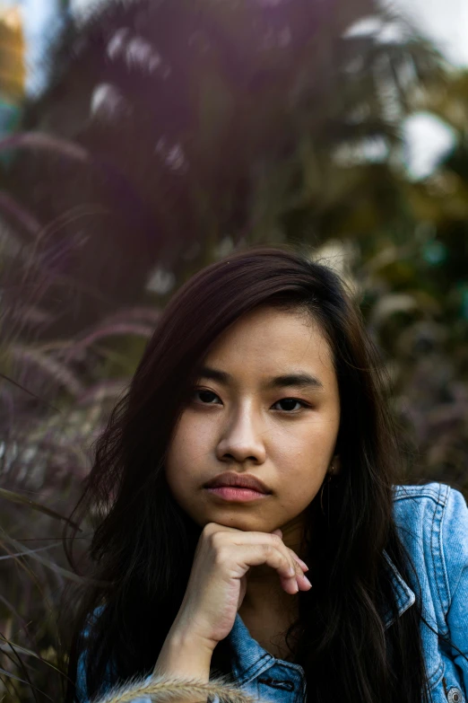 a woman sitting in the grass with her hand on her chin, a picture, by Robbie Trevino, unsplash, realism, south east asian with round face, 🤤 girl portrait, portrait soft low light, serious face