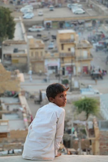 a boy sitting on a ledge looking over a city, inspired by Steve McCurry, happening, on an indian street, in a war - torn desert village, zoomed in shots, ignant