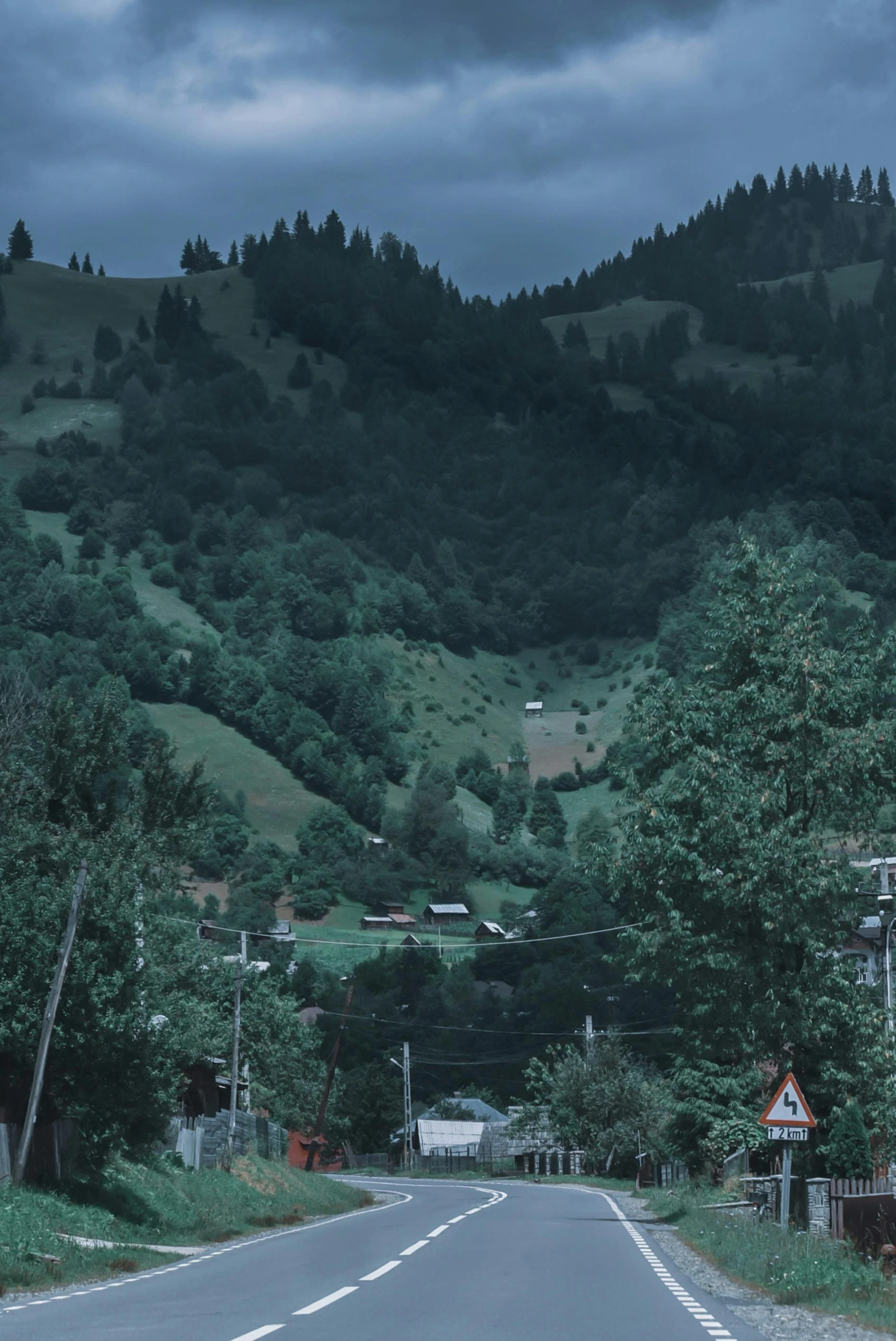 a man riding a skateboard down the middle of a road, inspired by Elsa Bleda, renaissance, ominous! landscape of north bend, russian village, hillside, background image