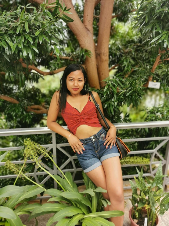 a woman sitting on a bench next to a tree, wearing a tank top and shorts, manila, standing in a botanical garden, ❤🔥🍄🌪