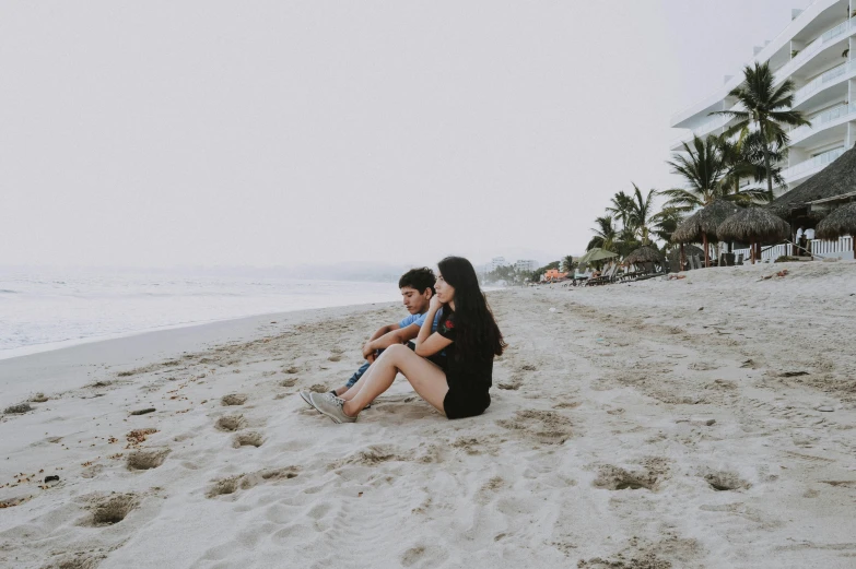 a couple of people sitting on top of a sandy beach, pexels contest winner, realism, teenage girl, mexico, slight overcast lighting, avatar image