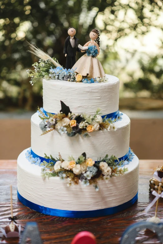 a wedding cake sitting on top of a wooden table, blue and white, figurines, zoomed out view, modeled