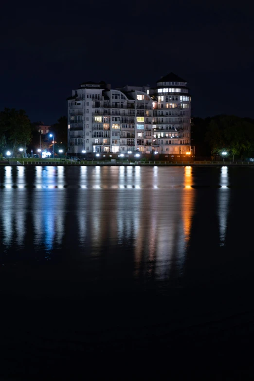 a large body of water with buildings in the background, during the night, lake house, full building, multiple stories