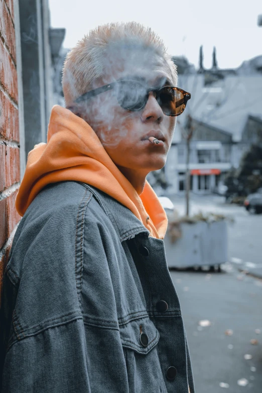 a man standing in front of a brick wall smoking a cigarette, a picture, trending on pexels, wearing orange sunglasses, in a hood, smoke around her, asian male