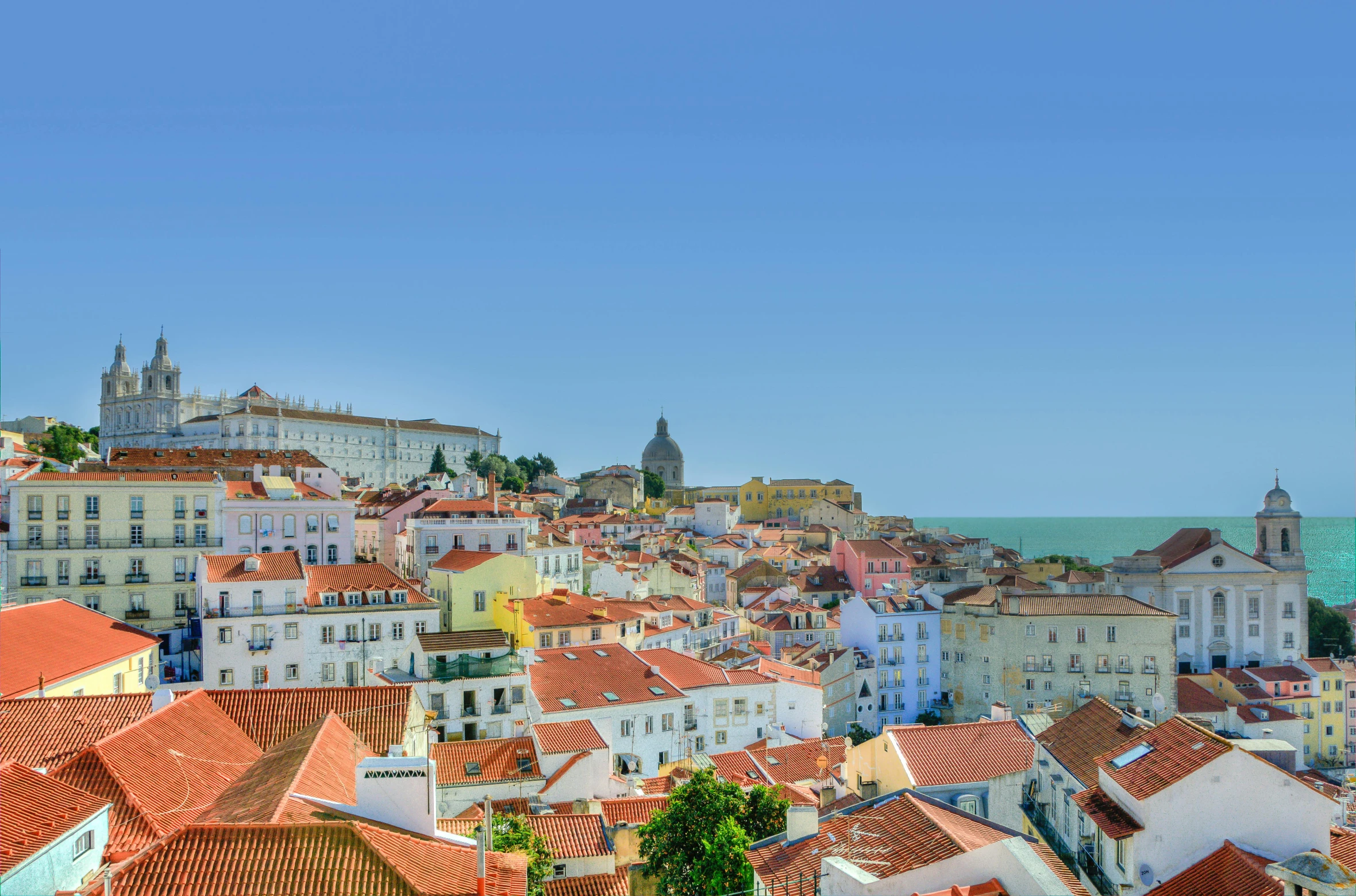 a view of a city from the top of a hill, inspired by Almada Negreiros, pexels contest winner, art nouveau, clear blue sky, square, multicolored, brown