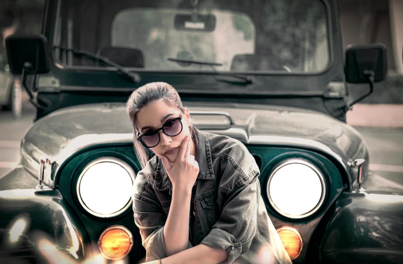 a woman sitting on the hood of a green jeep, inspired by mads berg, pexels contest winner, photorealism, wearing black glasses, indian super model, with cool headlights, grungy