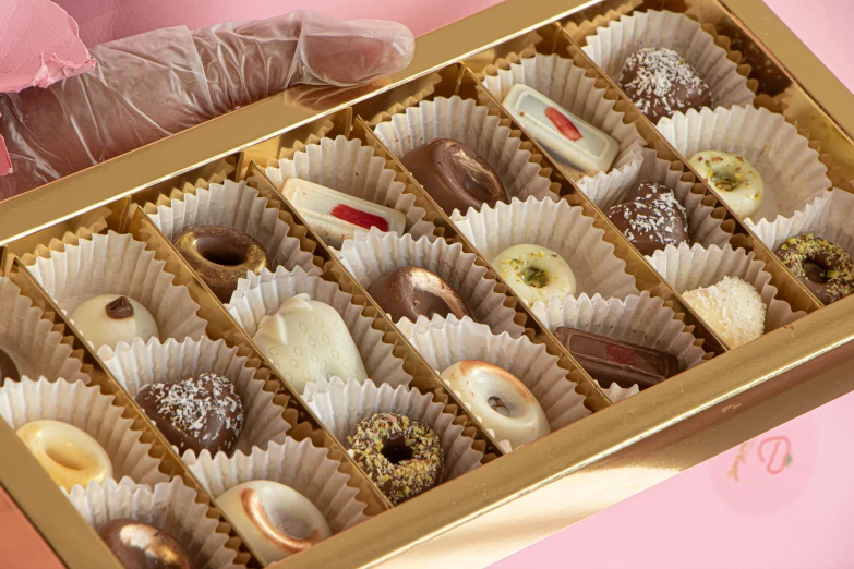 a box of assorted chocolates on a pink surface, sleek hands, gold colours, close up details, 4 0 0 0 samples