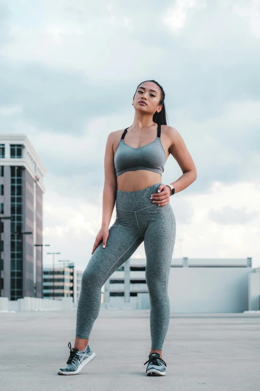 a woman in a sports bra top and leggings, by Robbie Trevino, trending on pexels, renaissance, mai anh tran, grey clothes, skies behind, full body hero