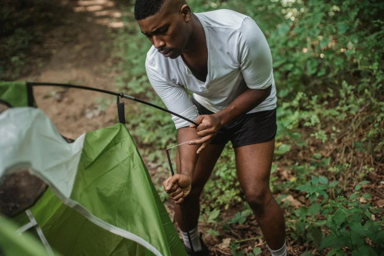 a man setting up a tent in the woods, pexels contest winner, man is with black skin, a green, lachlan bailey, injured