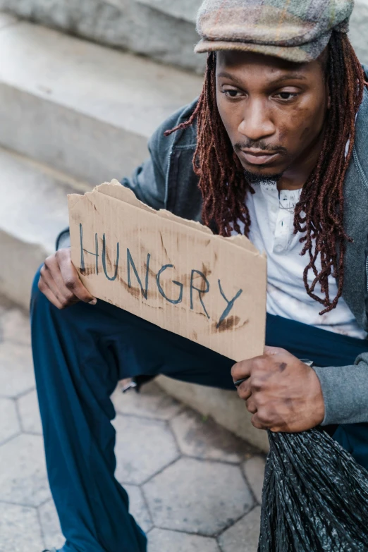 a man sitting on the steps holding a sign, by Matija Jama, trending on unsplash, renaissance, hungry, malnourished, playboi carti, a person standing in front of a