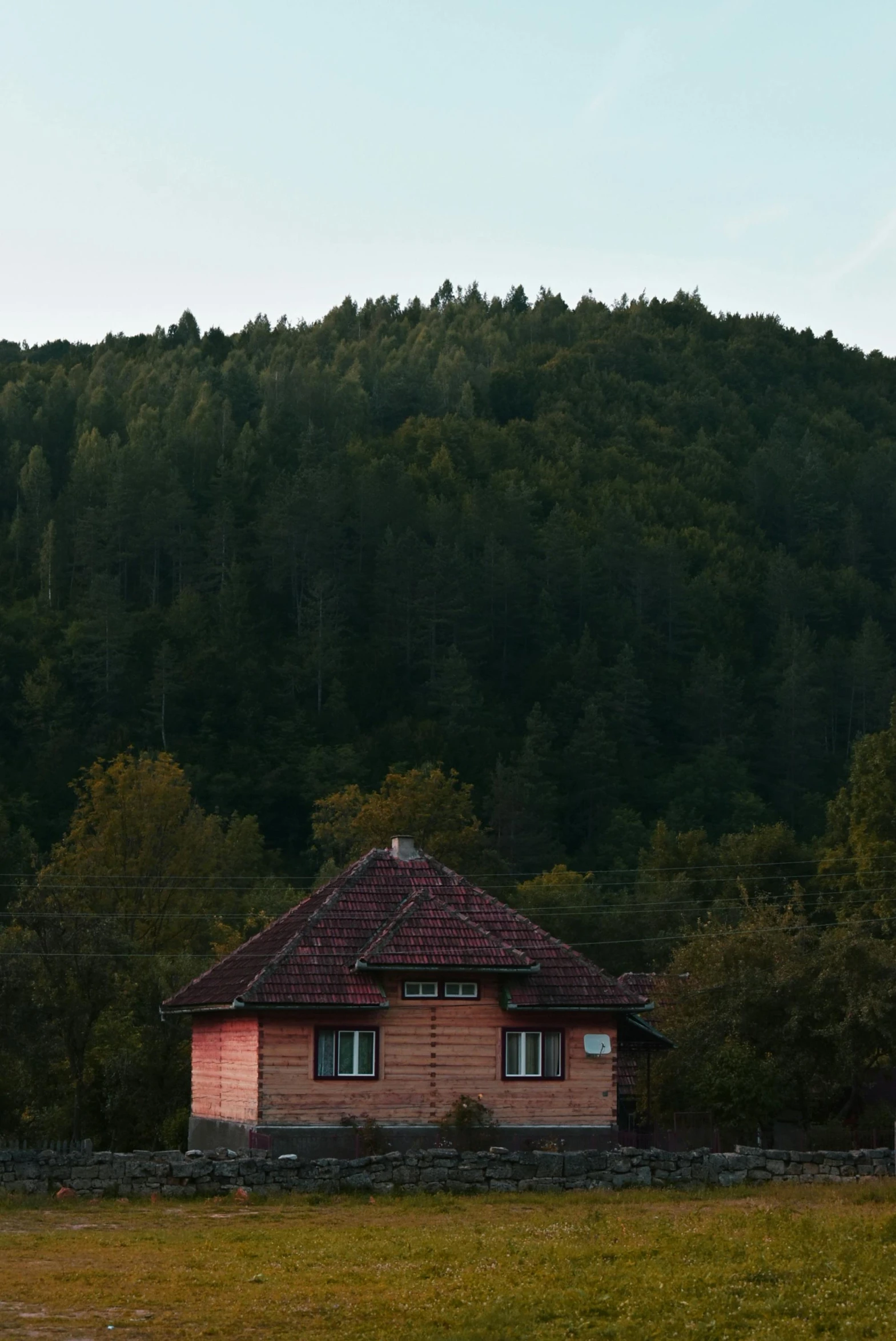 a house in the middle of a field with trees in the background, inspired by Edo Murtić, unsplash, carpathian mountains, late summer evening, rounded roof, portrait mode photo