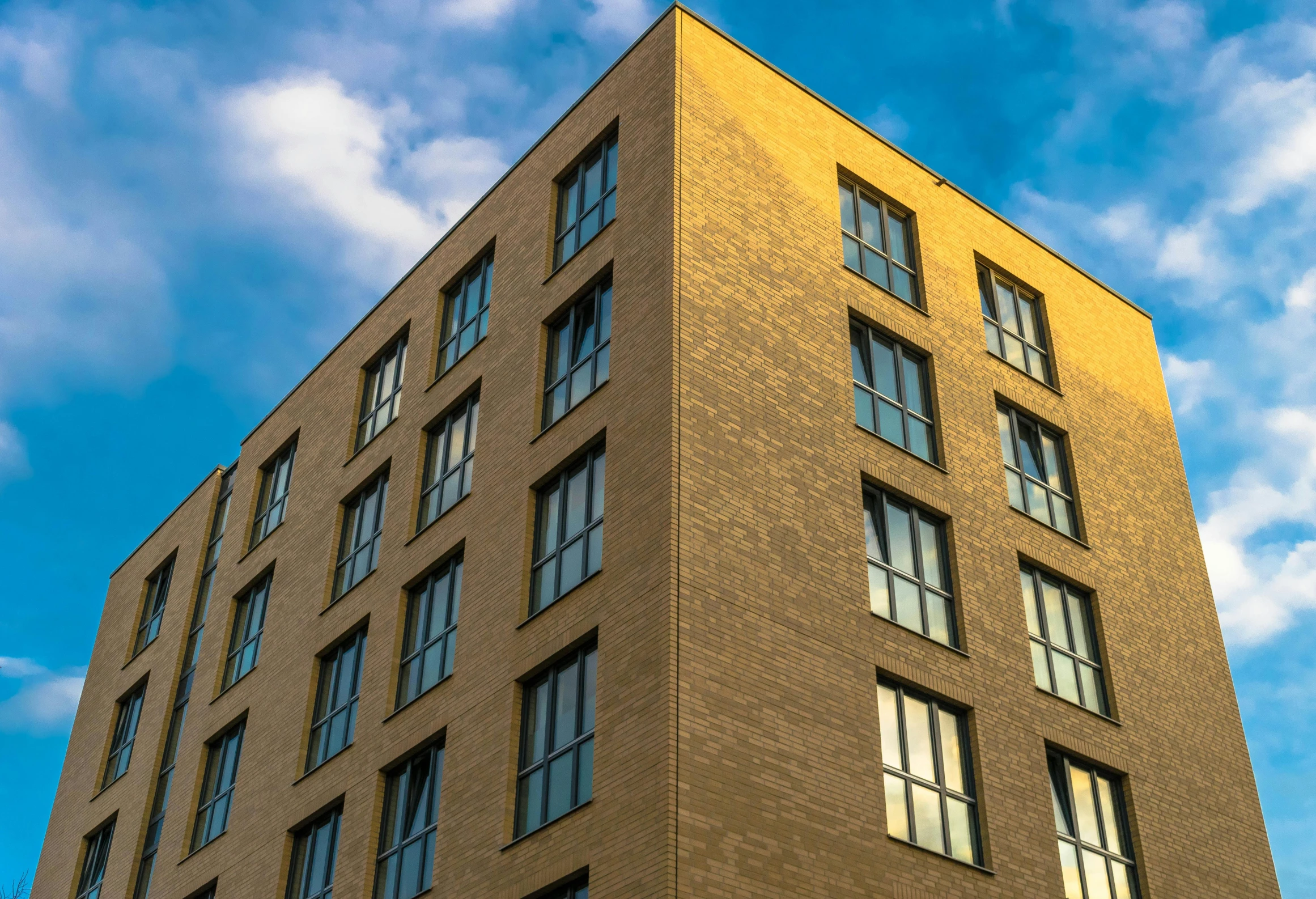 a tall brick building with lots of windows, inspired by Albert Paris Gütersloh, unsplash, modernism, gold, ten flats, a wooden, low angle