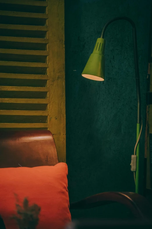 a red pillow sitting on top of a brown chair, by Elsa Bleda, unsplash, green lighting, emerging from a lamp, industrial colours, light inside the hut