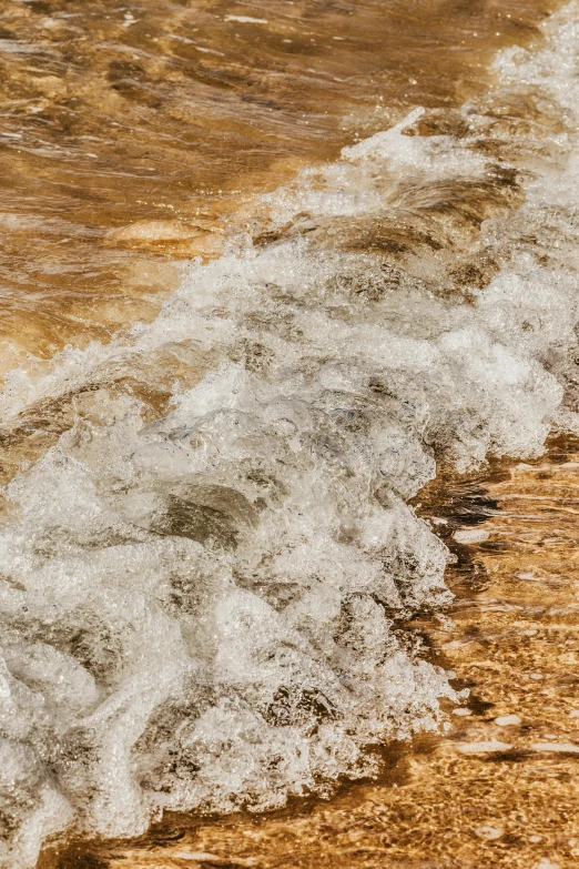 a man riding a surfboard on top of a sandy beach, rushing water, shades of gold display naturally, abstract photography, small river