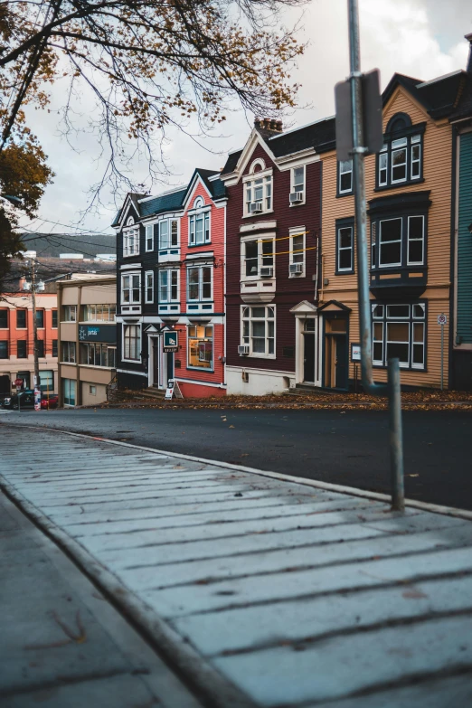 a red fire hydrant sitting on the side of a road, by Jessie Algie, pexels contest winner, visual art, colorful houses, built on a steep hill, in muted colours, proudly walking down the street