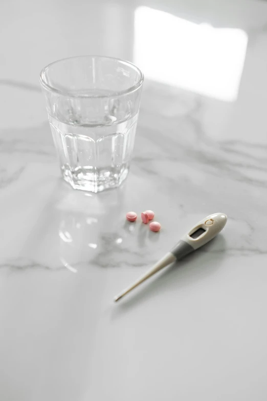a glass of water and a thermometer on a table, a digital rendering, by Anita Malfatti, trending on pexels, hyperrealism, pills, while marble, contracept, grey