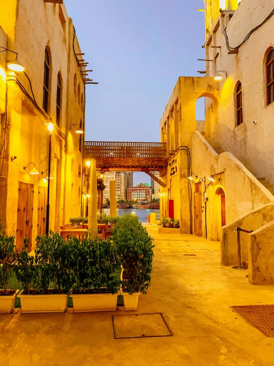 a narrow street is lit up at night, tanned ameera al taweel, at dusk at golden hour, big arches in the back, canals