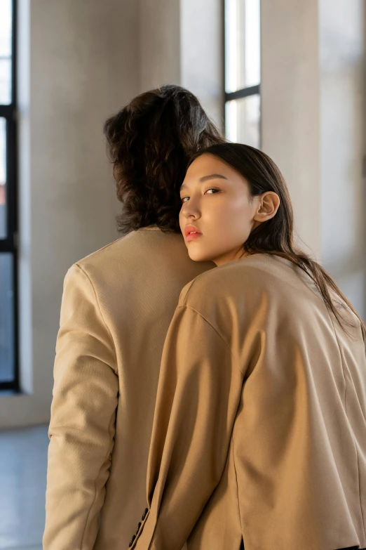 a man and a woman standing next to each other, inspired by Wang Duo, trending on pexels, visual art, light brown coat, arm around her neck, young asian woman, rear-shot