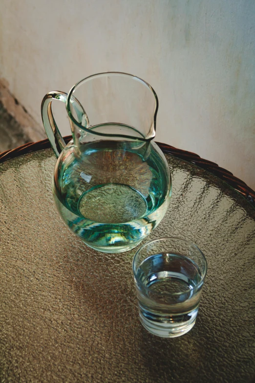 a pitcher and a glass of water on a table, inspired by Elsa Bleda, renaissance, teal energy, round-cropped, worn, turkey