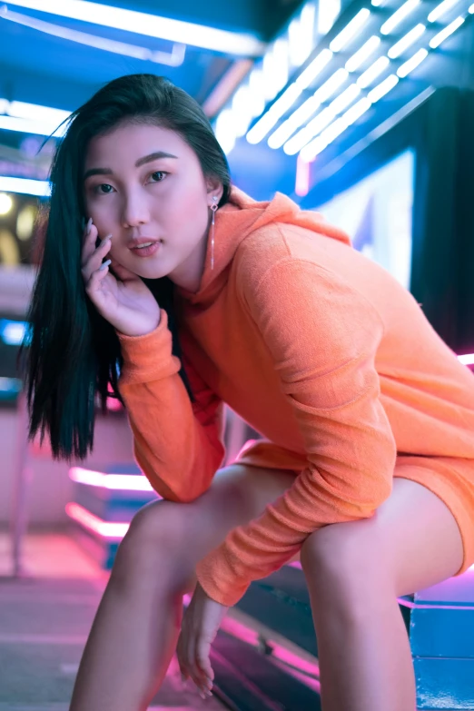 a woman sitting on a bench talking on a cell phone, an album cover, inspired by Wang E, pexels contest winner, long orange sweatshirt, star trek asian woman, attractive pose, gif