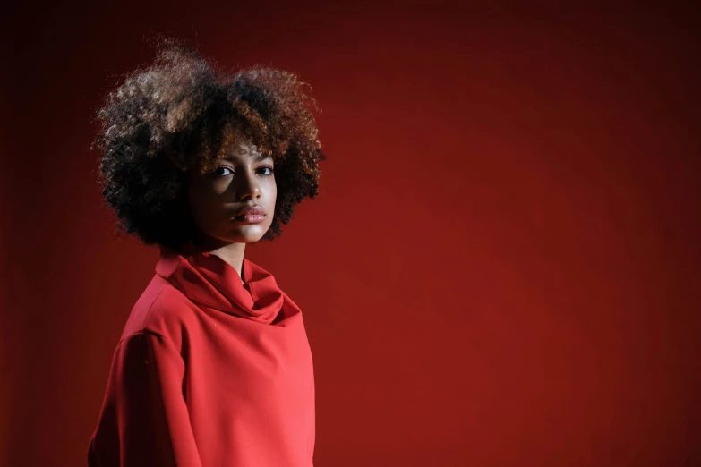 a woman standing in front of a red wall, inspired by Clifford Ross, pexels contest winner, afrofuturism, wearing a red turtleneck sweater, curly haired, girl wears a red dress, photographed for reuters