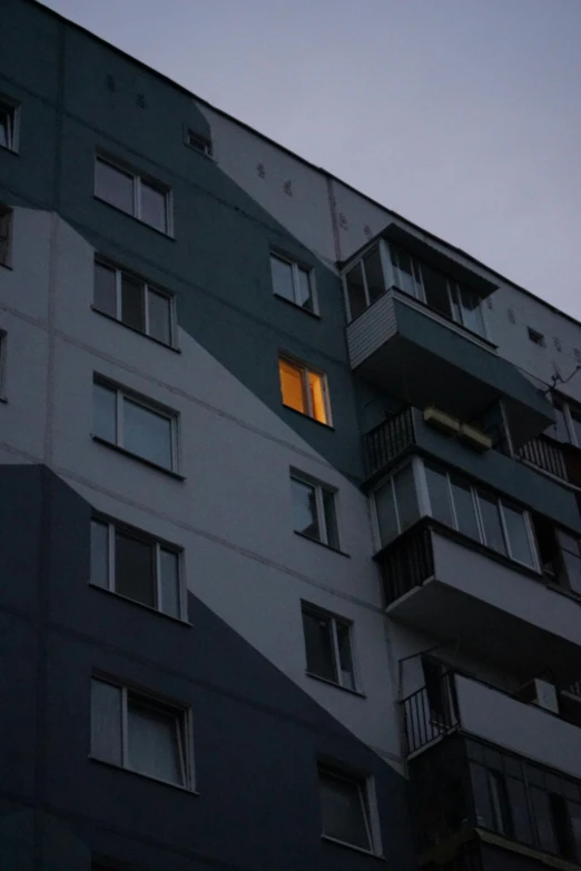 a tall building with windows lit up at night, an album cover, by Attila Meszlenyi, moscow, low quality photo, old apartment, low iso